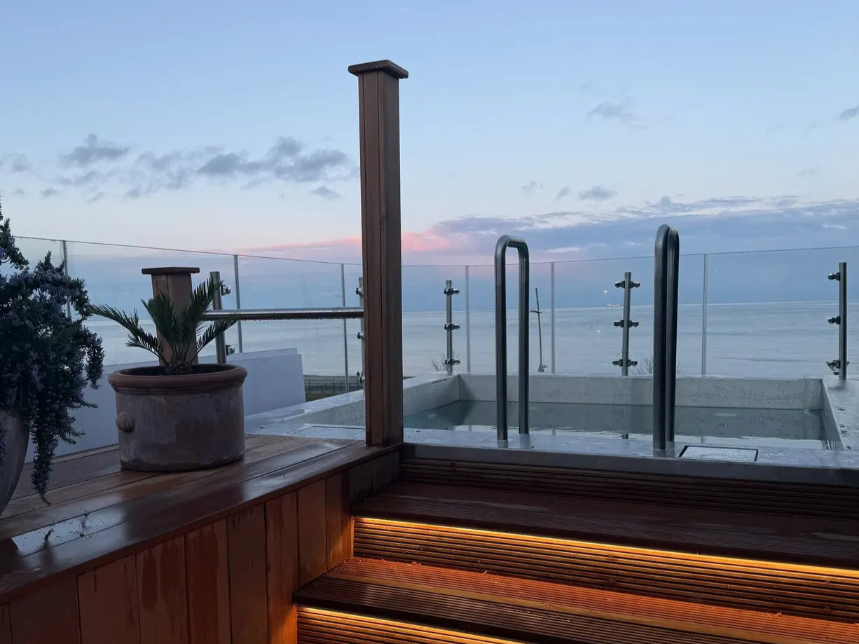 Outdoor setting with wooden steps leading to a pool area overlooking the ocean at dusk.