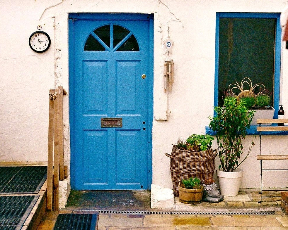 Blue door with plants and a clock on a white wall