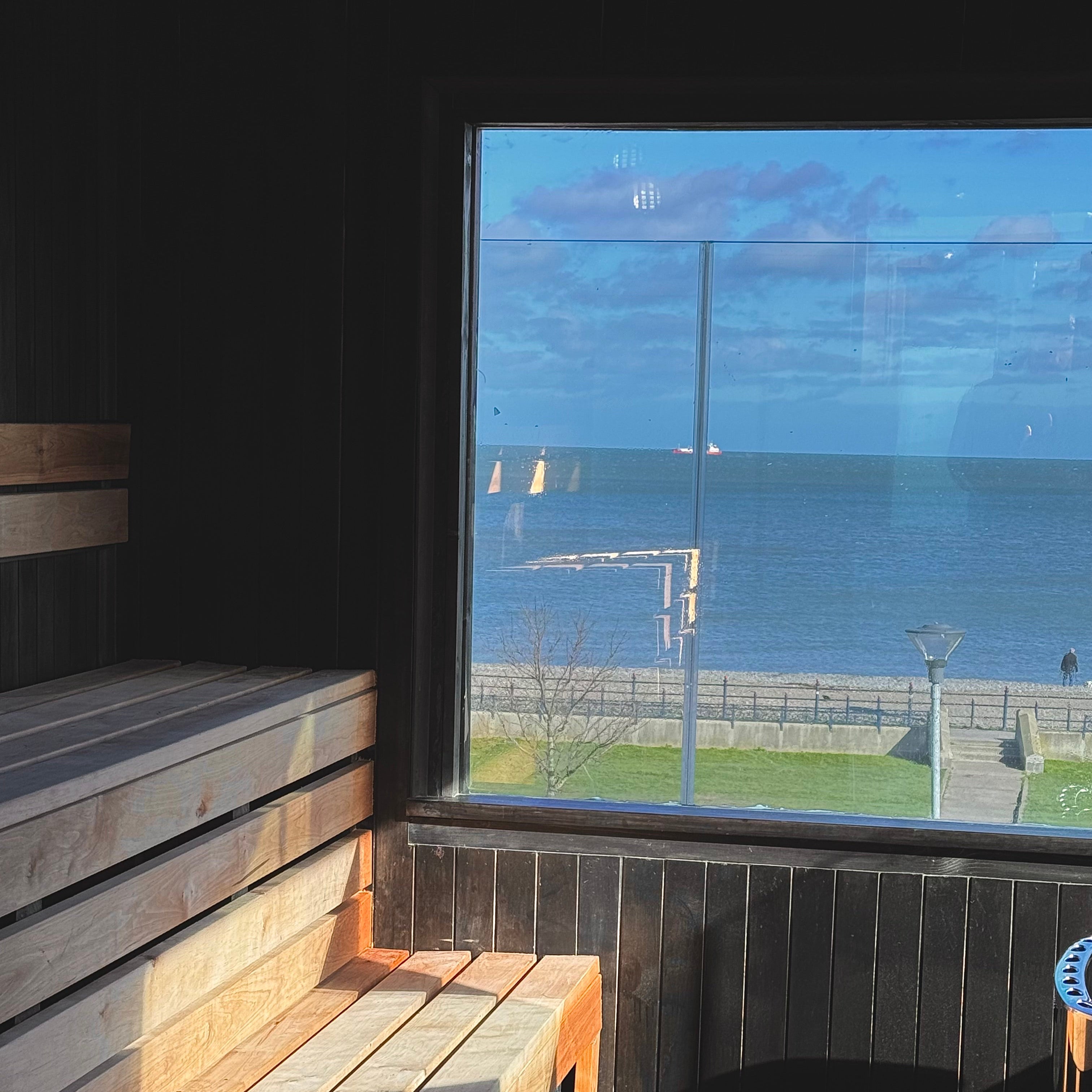 Wooden bench inside a sauna with a large window overlooking a coastal view.