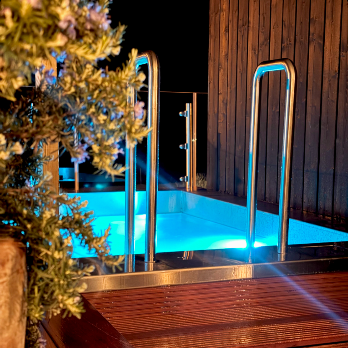 Wooden deck area with a pool at night