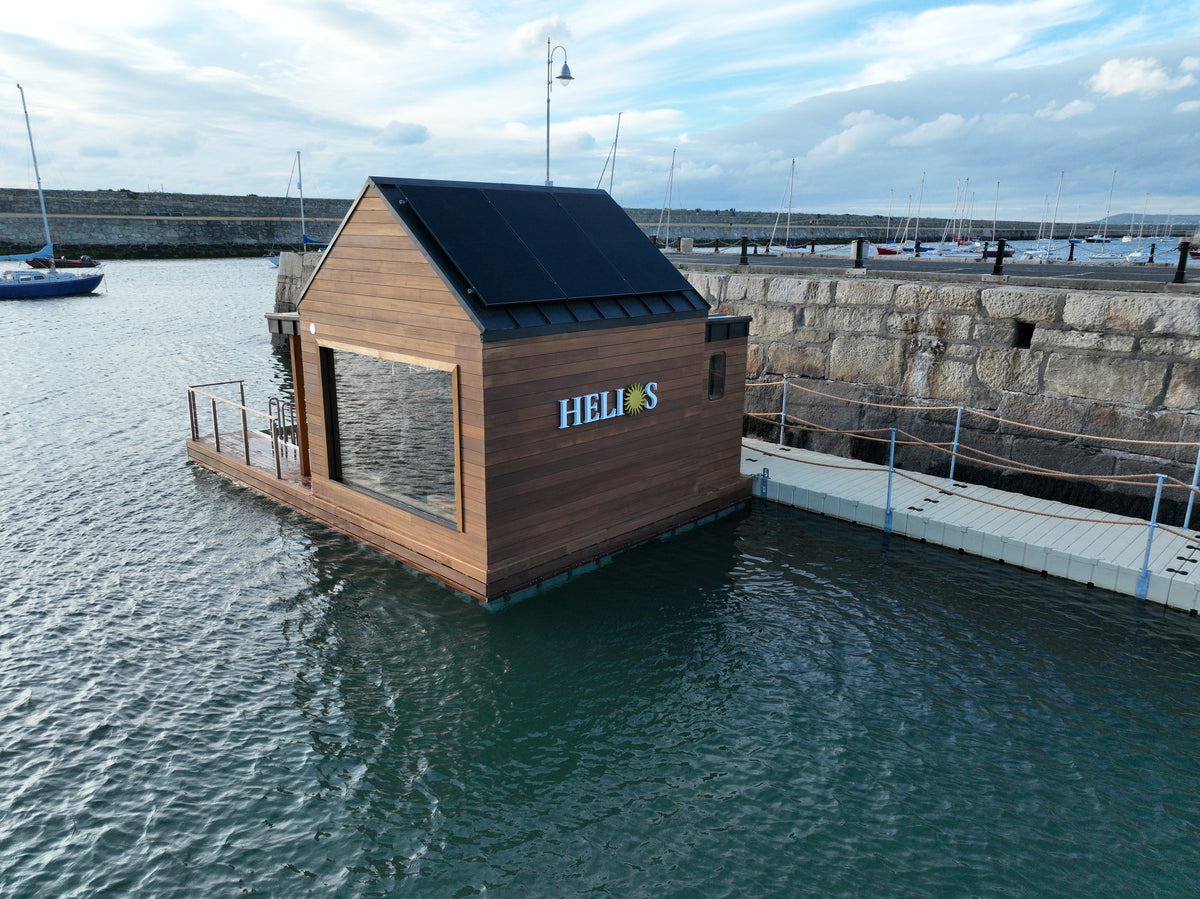 Helios’s timber sauna floating in the harbour, with its deck beside open water.